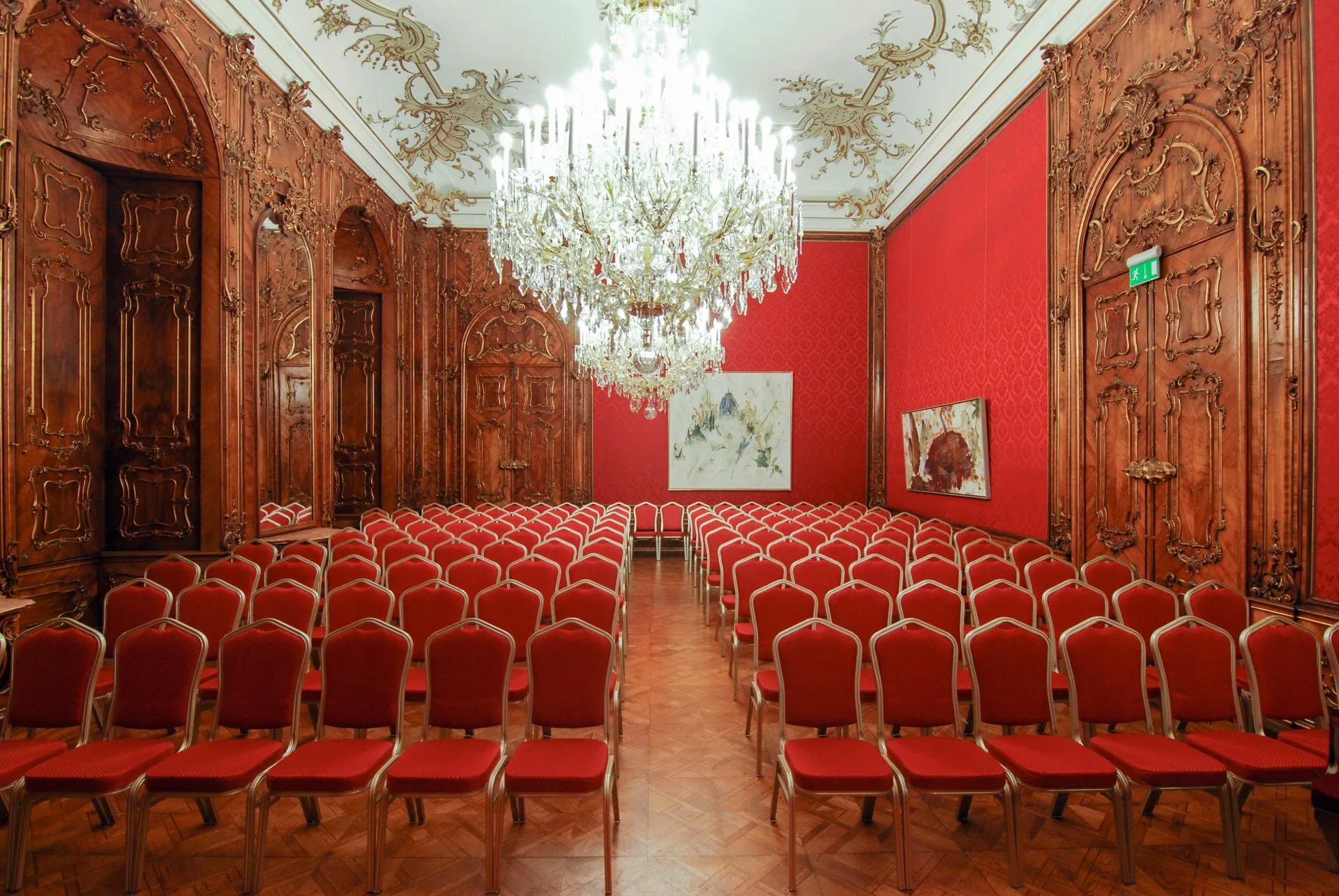 The Roter Salon set for a concert: rows of red chairs either side of a centre aisle under the crystal chandelier, carved walnut doors along one wall.