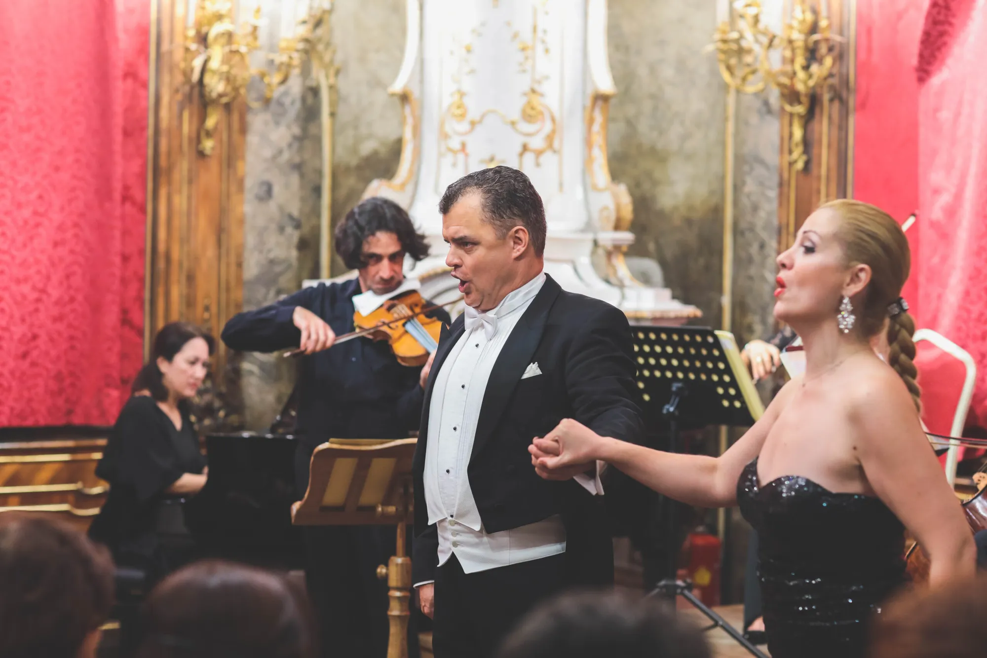 A baritone and a soprano singing a duet in front of the orchestra, the violinist and pianist behind them.