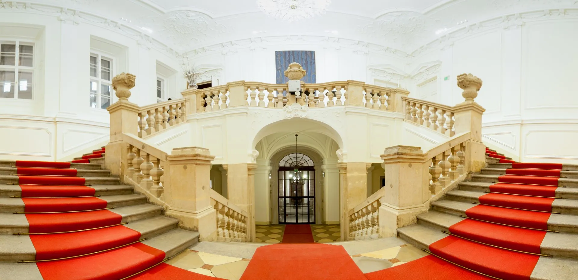 The palace’s double staircase under its stucco ceiling, red carpet running up both flights to the piano nobile.