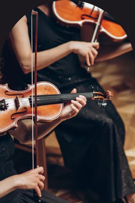 Two violinists of the ensemble mid-phrase, bows drawn, seen from the shoulders down.