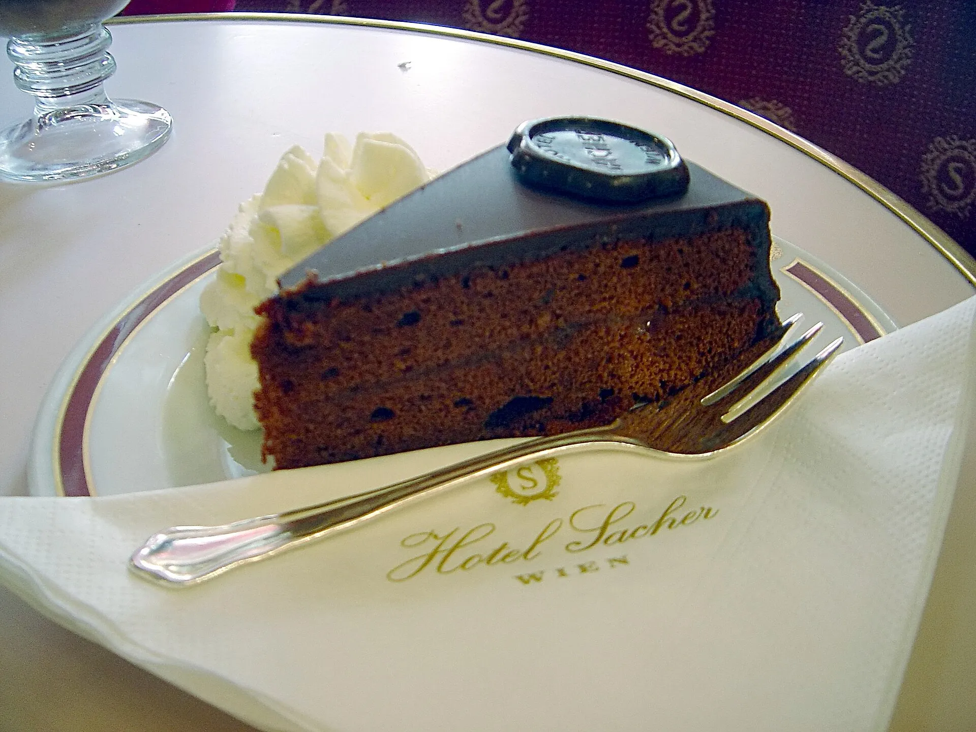 A slice of Sachertorte with whipped cream on a café plate