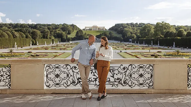 Two visitors above Schönbrunn looking at a phone, the Gloriette behind them