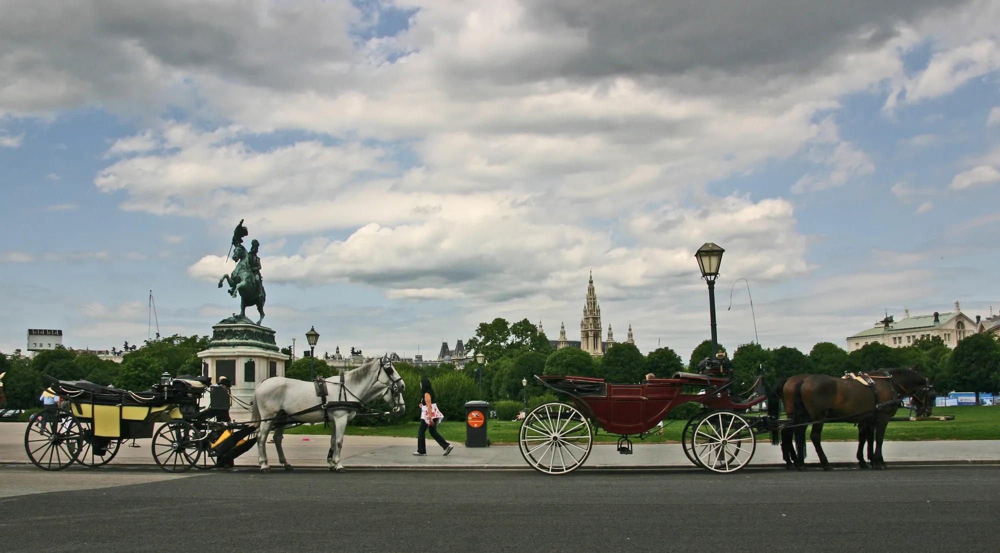 Two carriages crossing Heldenplatz towards the Ring, the Rathaus tower on the skyline.
