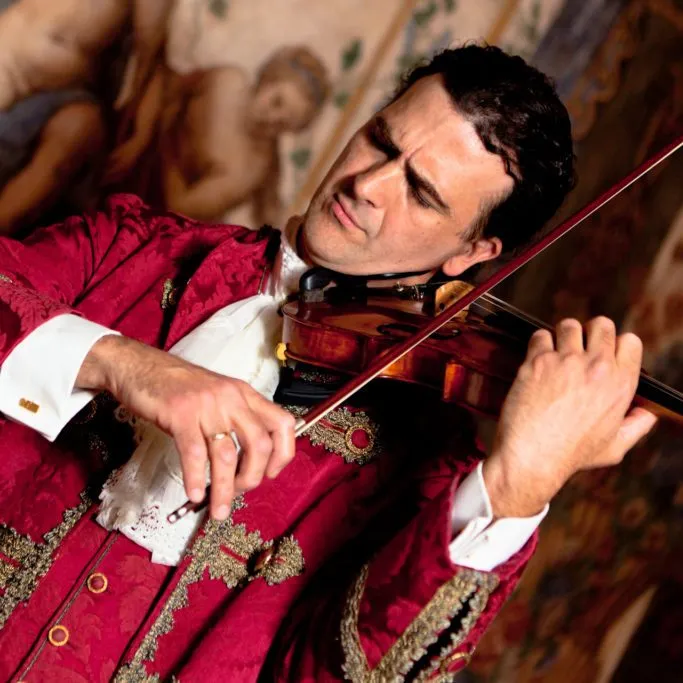 Claudio Bentes, founder and artistic director, playing the violin in a red brocade coat.