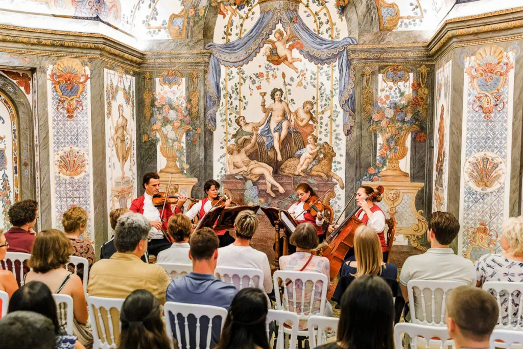 The room from a seat in the audience: four players an arm’s length away against the frescoed wall.