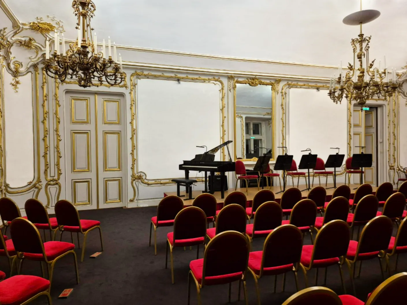 The White-and-Gold Room set for a concert: red chairs facing a grand piano between the white-and-gold panelled walls.