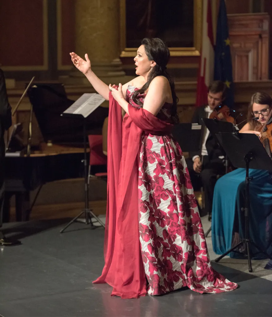 A soprano in a red gown singing an aria with the orchestra.