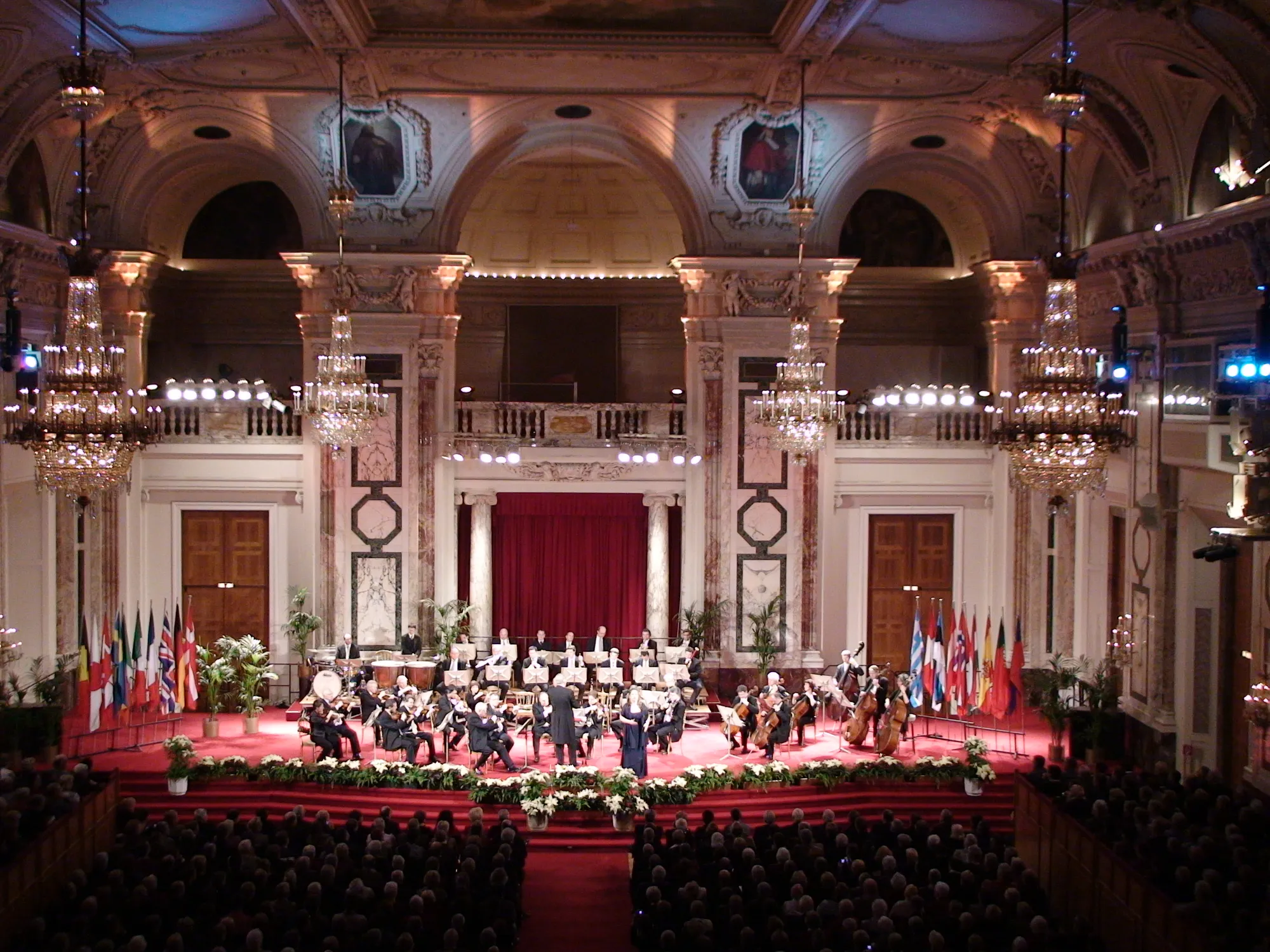 The Festsaal of the Hofburg set for a concert: marble columns, chandeliers and an orchestra on the stage.