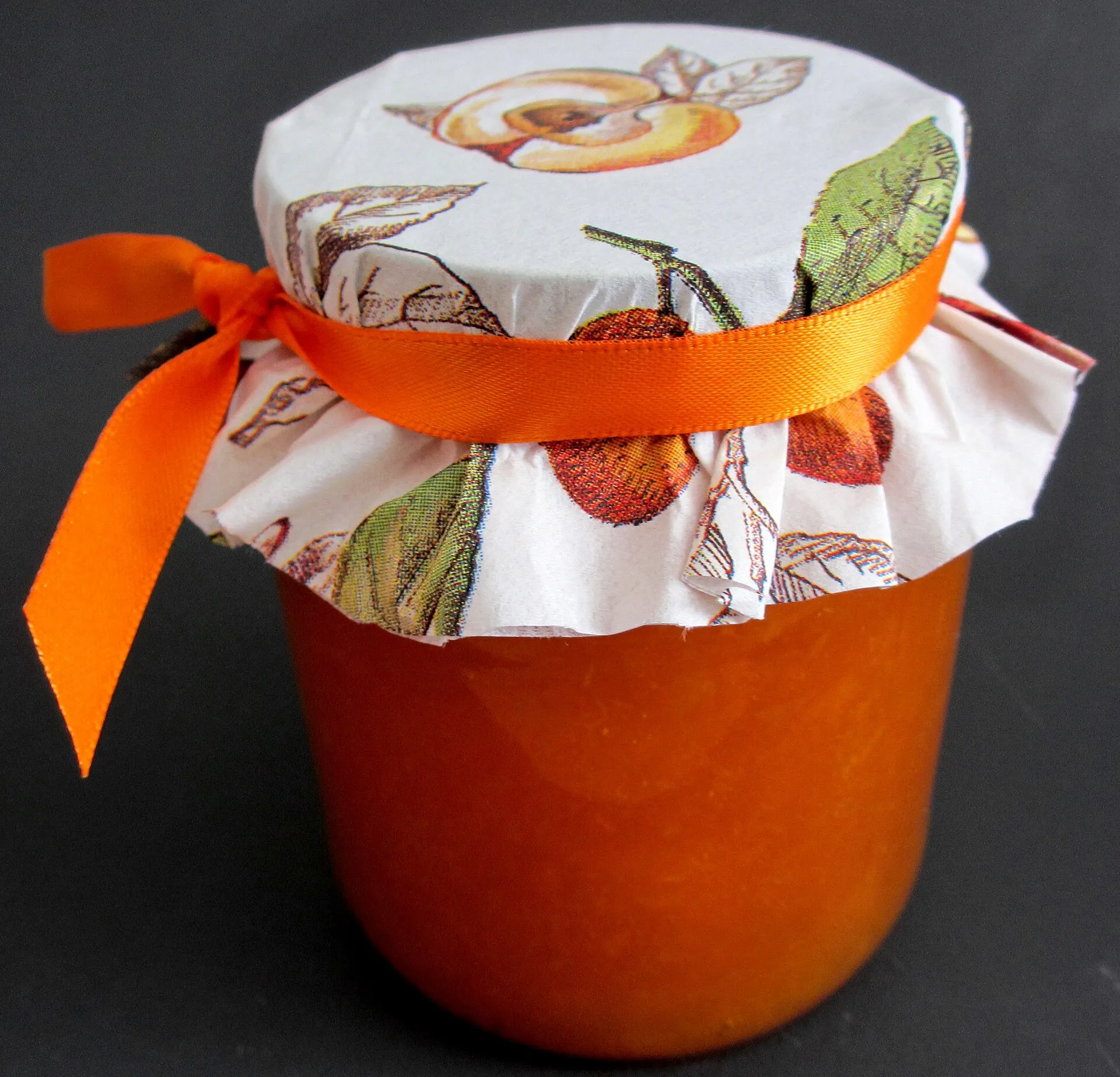 A jar of bright orange apricot jam with a cloth-covered lid