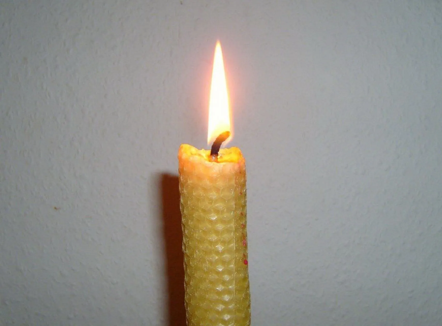 A rolled beeswax candle, lit, the honeycomb pattern of the sheet showing