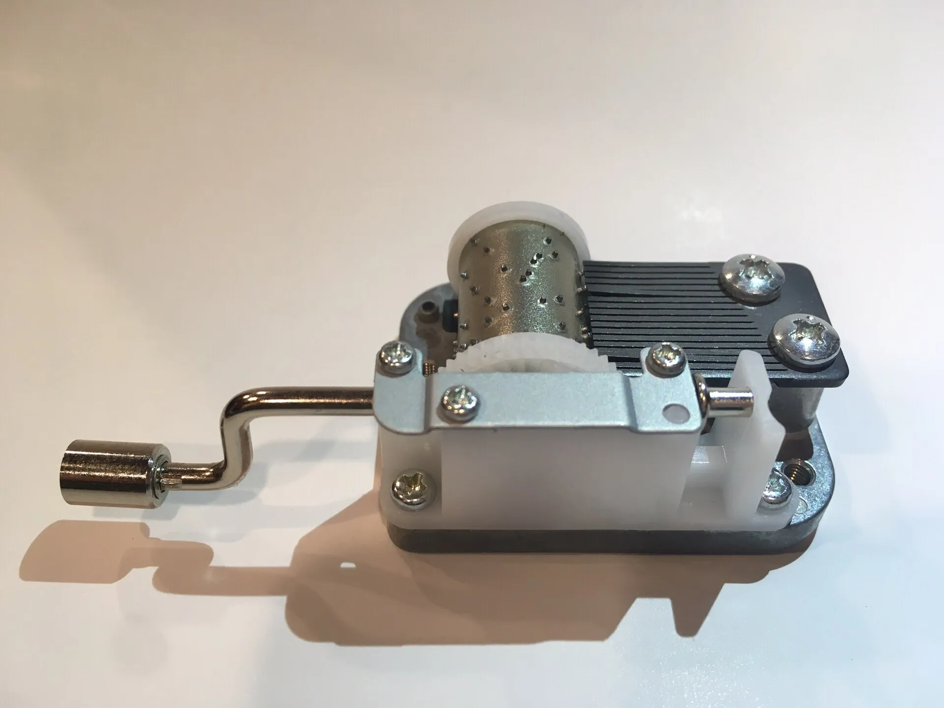 A small hand-cranked music box movement: the pinned cylinder and the steel comb