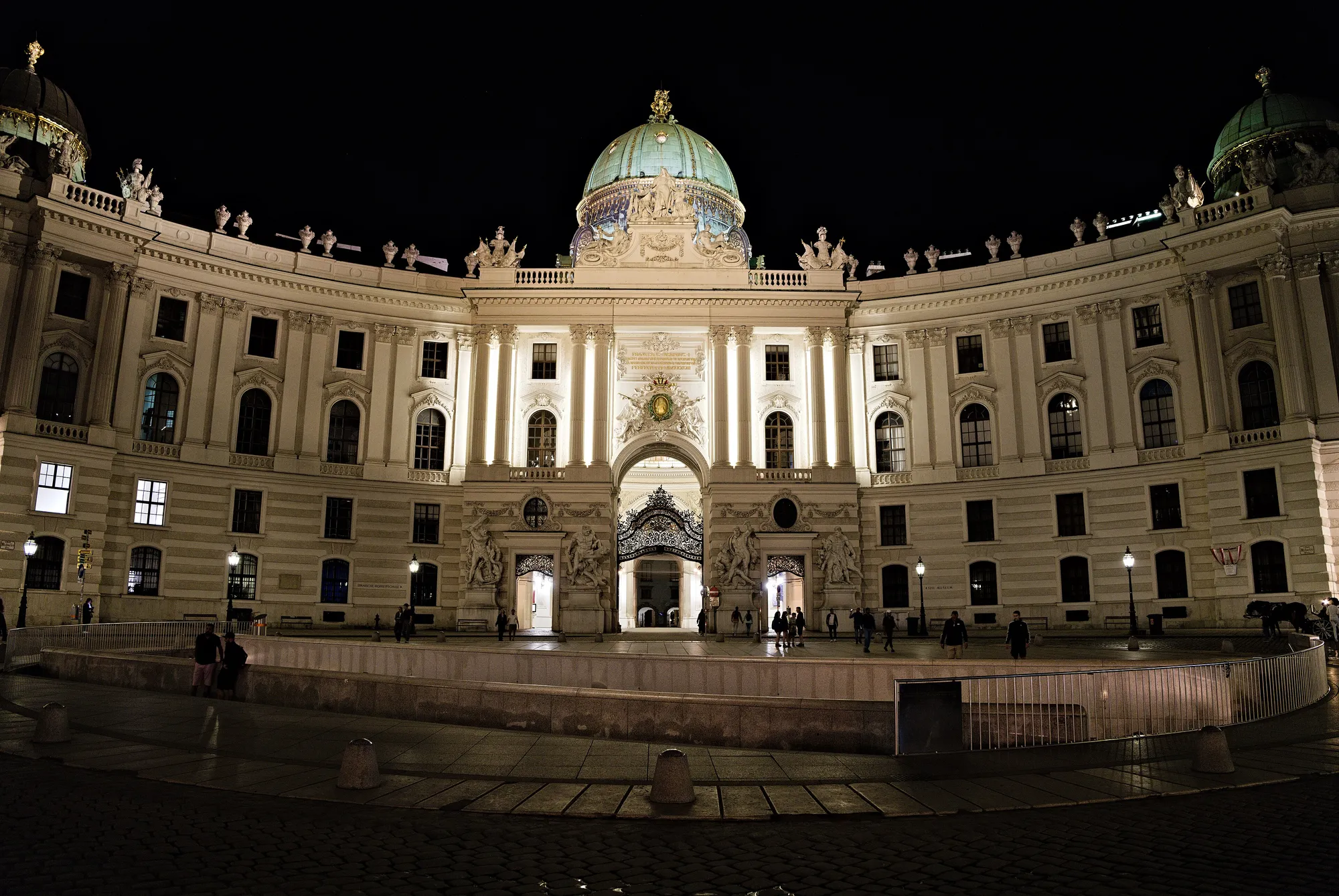 Michaelerplatz at night, the floodlit Hofburg gate above the square.