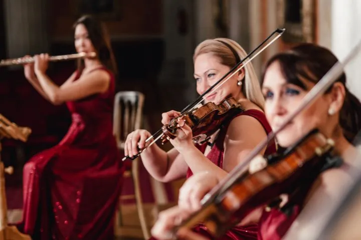 Flute and two violins of the Wiener Residenz Orchester, the players in red gowns.