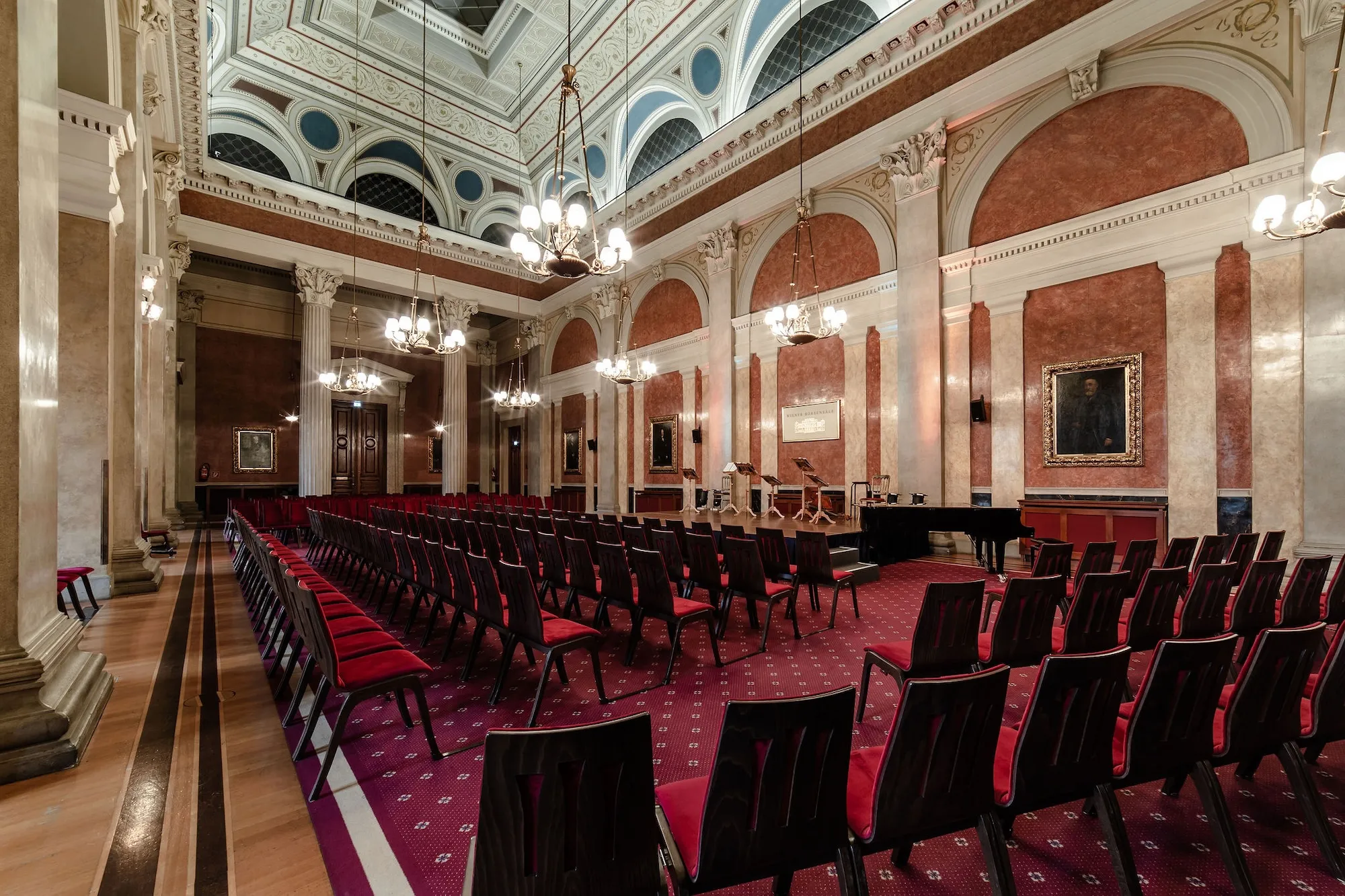 The Festsaal of the Palais alte Börse set for a concert: rows of red chairs beneath the chandeliers, the grand piano beside the podium.