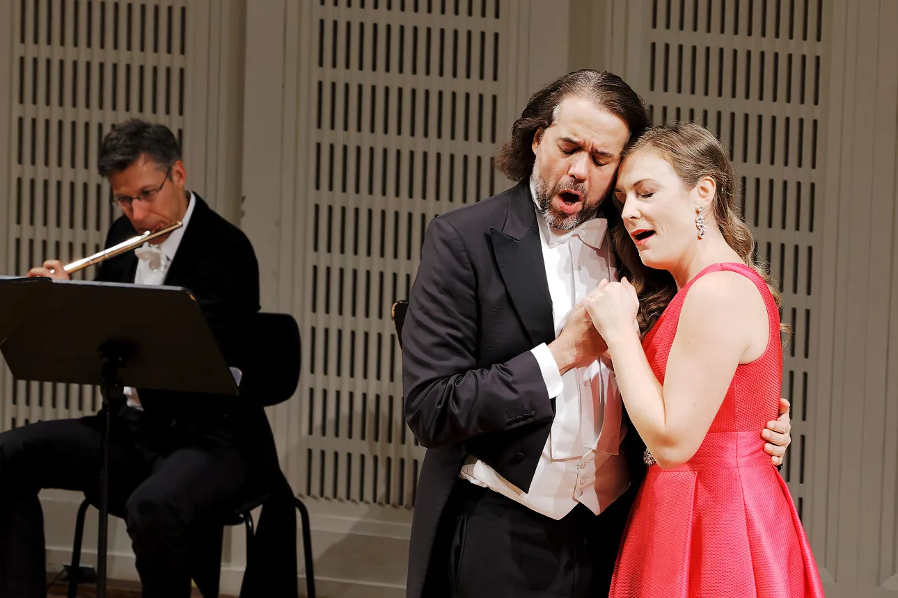 A soprano and a baritone singing a duet, the flautist of the ensemble behind them.